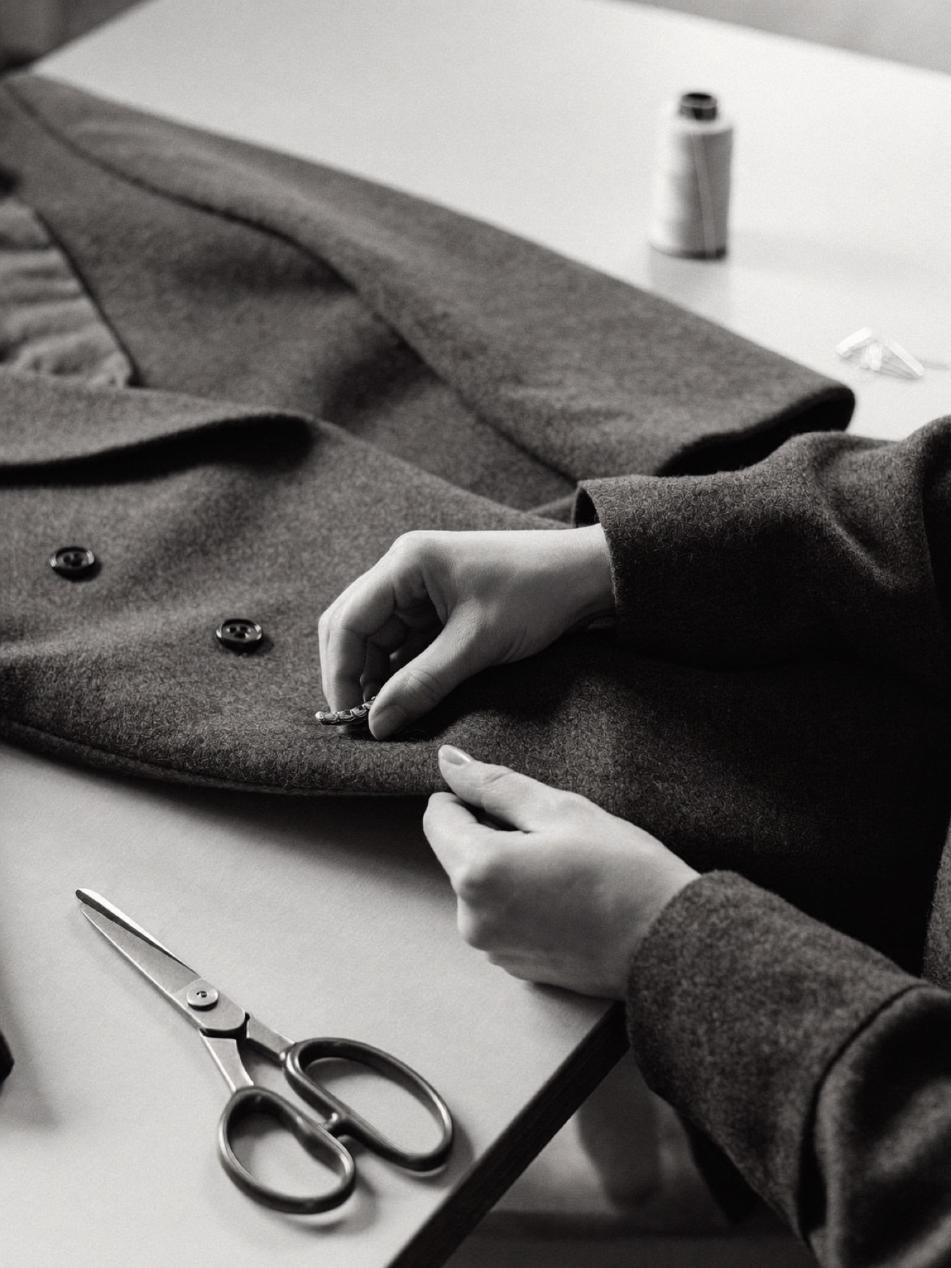 Hands finishing the hem of a wool coat on an atelier table